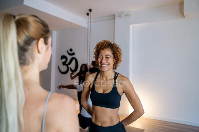 Fröhliche multirassische Frauen in Sportbekleidung stehen im Yoga-Studio und reden nach dem Unterricht miteinander — Stockfoto