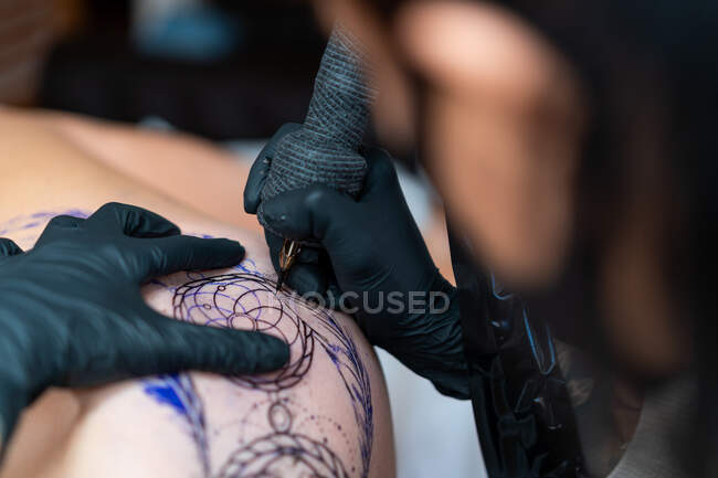 Татуировщица в маске для лица с татуировкой машины на теле неузнаваемого клиента в салоне — стоковое фото