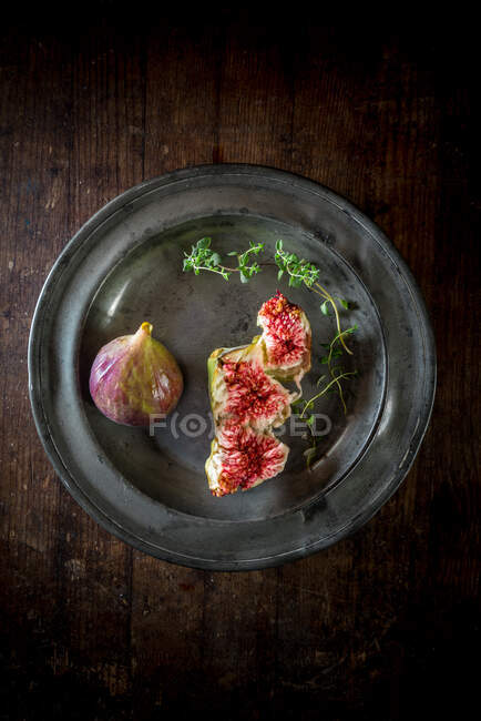 Vue aérienne de savoureuses tranches de figue mûre avec des brins de thym aromatiques sur une assiette sur une surface en bois — Photo de stock