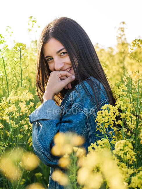 Delighted young brunette in jacket laughing merrily looking at camera on blooming rapeseed field on sunny day — Stock Photo