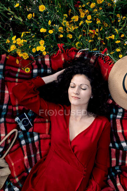 Top view of tender female with closed eyes touching hair while lying on checkered blanket with aged photo camera in field — Stock Photo