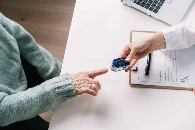 Top view of crop unrecognizable doctor measuring blood oxygen of patient with heart rate monitor at table with stethoscope in clinic — Stock Photo