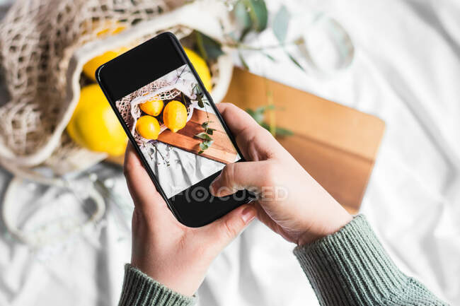 Вид зверху врожаю невідомий людина торкається екрану мобільного телефону, роблячи фото лимонів на обробній дошці — стокове фото