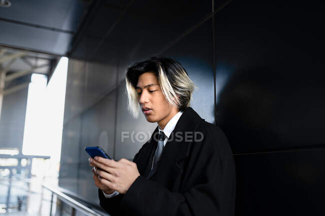 Jeune dirigeant masculin asiatique attentif dans les vêtements formels de messagerie texte sur téléphone mobile en plein jour — Photo de stock