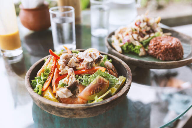 Délicieuse salade de poulet sain avec des tomates et des capsicums servis sur une table en verre près de l'assiette avec du riz noir sain dans un restaurant asiatique — Photo de stock