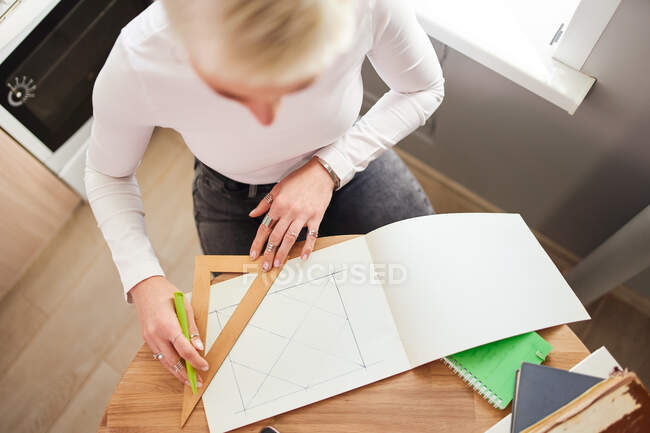 Зверху врожаю невизначена жінка-астролог малює на папері з трикутником і ручкою за столом — стокове фото
