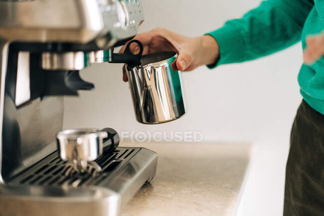 Cultiver une personne méconnaissable avec une cruche en métal préparer le café avec une machine professionnelle à la table dans la maison — Photo de stock