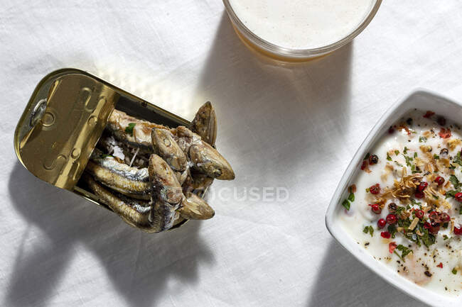 Blick von oben auf Sardellen in Dosen serviert in weißen Tisch mit Glas schäumendes Bier und weiße Gazpacho-Suppe — Stockfoto