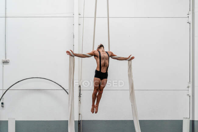 Esportista forte muscular de corpo inteiro em shorts realizando exercício em sedas aéreas no moderno centro de fitness leve — Fotografia de Stock