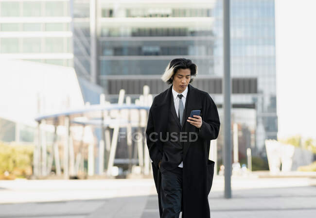 Jovem bem vestido étnico masculino executivo navegando no celular na rua da cidade olhando para a tela — Fotografia de Stock