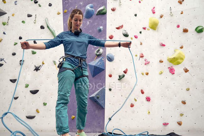 From below of female alpinist preparing ropes and harness for climbing in modern bouldering gym — Stock Photo