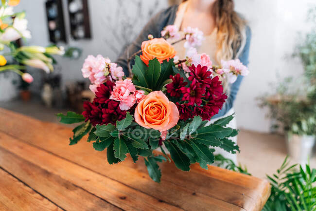 Невпізнавана молода самиця флорист з довгим хвилястим волоссям в повсякденному одязі і фартух організовує елегантний букет троянд і різні квіти в магазині. — стокове фото