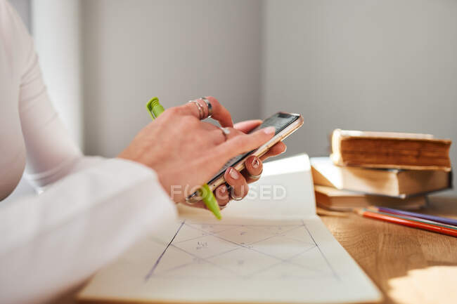 Side view of anonymous female astrologist using cellphone at home — Stock Photo