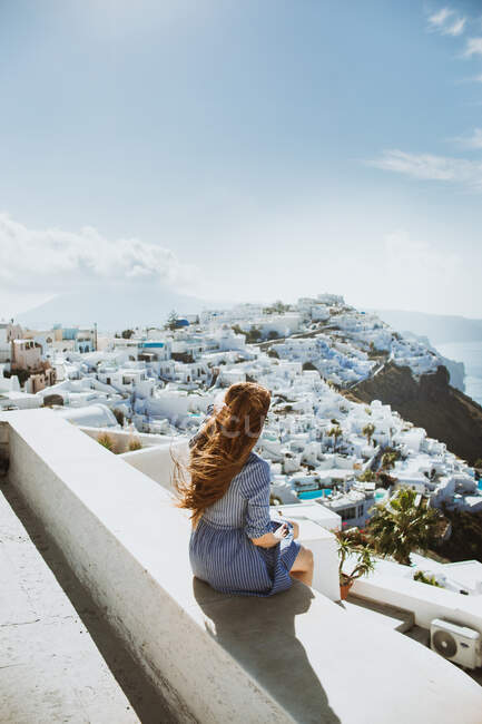 Vista posteriore di una viaggiatrice irriconoscibile che ammira l'Oia Village sull'isola di Santorini in una giornata ventosa in Grecia — Foto stock