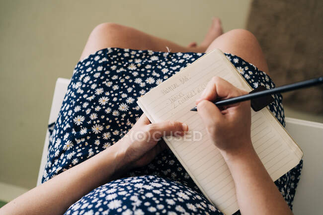 Зверху вагітна жінка сидить на комоді і пише нотатки — стокове фото