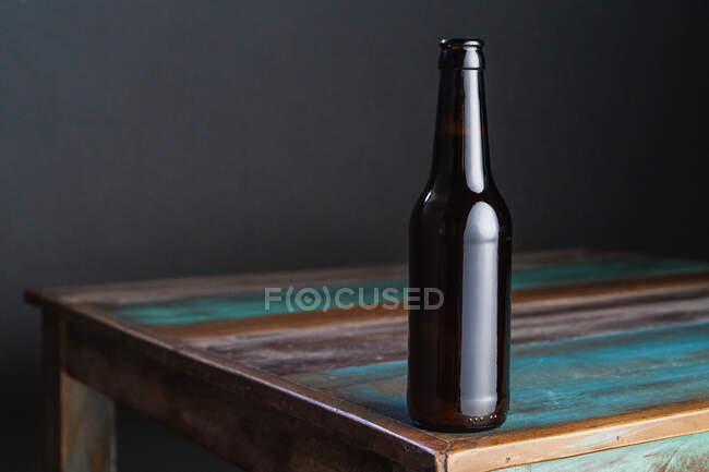 Темна скляна пляшка алкогольного напою на пофарбованому дерев'яному столі квадратної форми в домашніх умовах — стокове фото