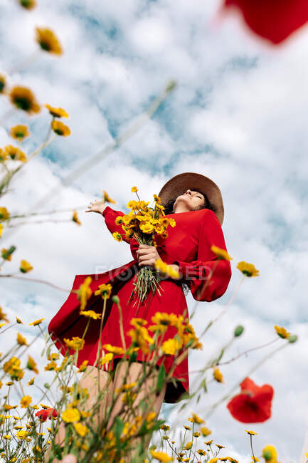De baixo da fêmea elegante no chapéu entre flores florescendo no campo rural no dia de verão — Fotografia de Stock