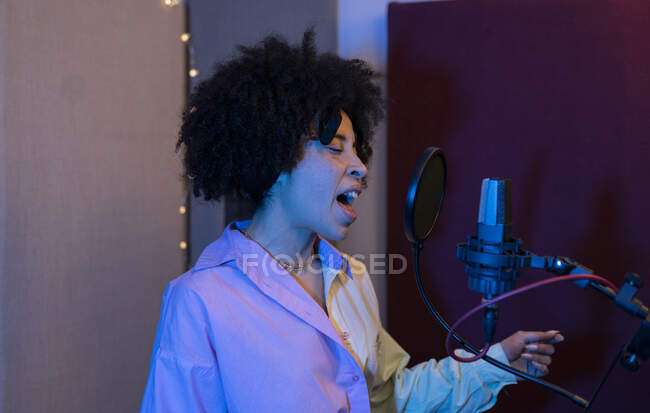 Cantante nera che canta contro il microfono con filtro pop in piedi con mano sull'anca e gli occhi chiusi in studio sonoro — Foto stock