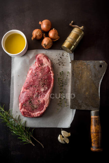 Top view of uncooked meat piece with seasonings between fresh rosemary sprigs and garlic cloves on dark background — Stock Photo