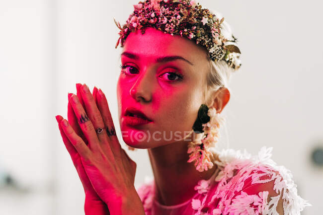 Elegant young female in white wedding gown with jewelry wreath looking at camera in studio with neon illumination — Photo de stock
