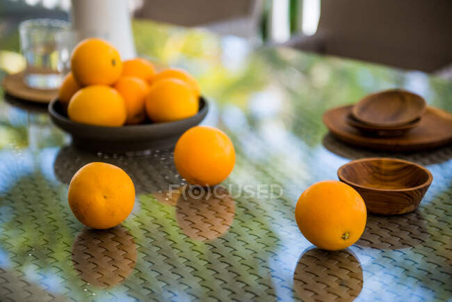 Высокий угол спелых свежих мандаринов, разбросанных по плетеному столу со стеклянным верхом возле деревянных чаш на веранде в солнечный день — стоковое фото