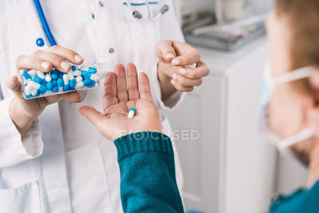 Cropped unrecognizable female medic in uniform and disposable mask preparing medications for anonymous elderly patient during consultation in clinic — Stock Photo