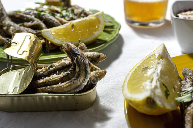 From above of delicious fried anchovies served on plate and cat with lemon and placed on white table with glass of beer — Photo de stock