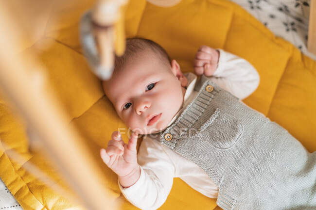 From above of cute little child in knitwear lying on soft bed while looking up in house — Stock Photo