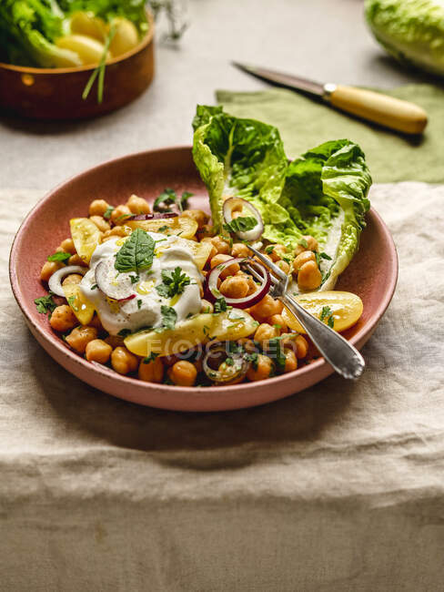 Von oben appetitanregende Kichererbsen mit Burrata-Käse und verschiedenen Gemüse und Kräutern auf dem Teller auf dem Tisch serviert — Stockfoto