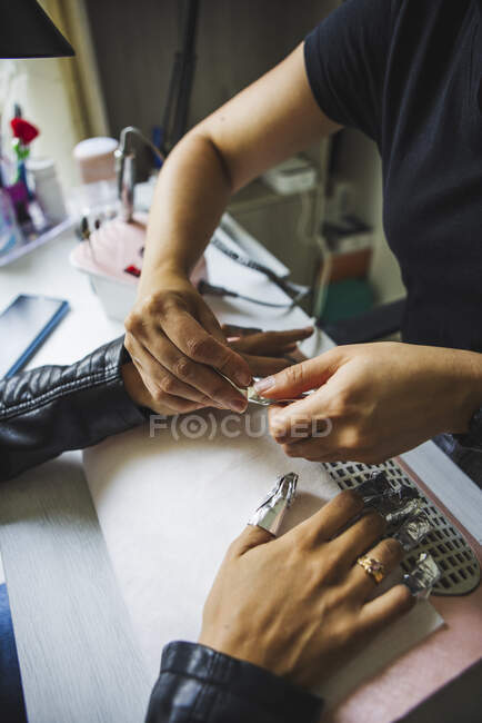 From above crop unrecognizable master removing gel nail polish of female client with foil sitting at table in spa center - foto de stock