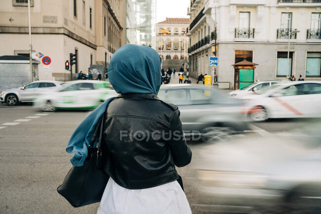 Back view of anonymous Muslim female in hijab standing near road with busy traffic in rush hour — Stock Photo