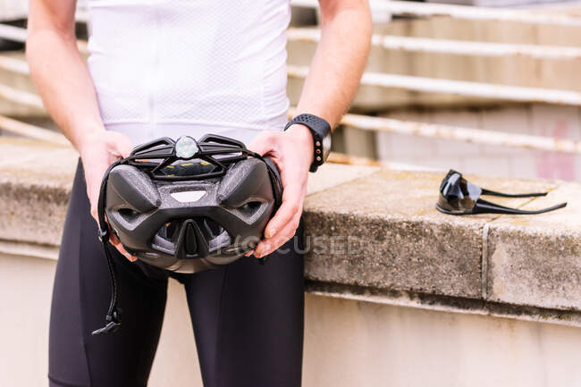 Неузнаваемый мужчина-велосипедист в шлеме и умные часы против современных солнцезащитных очков на заборе в городе — стоковое фото