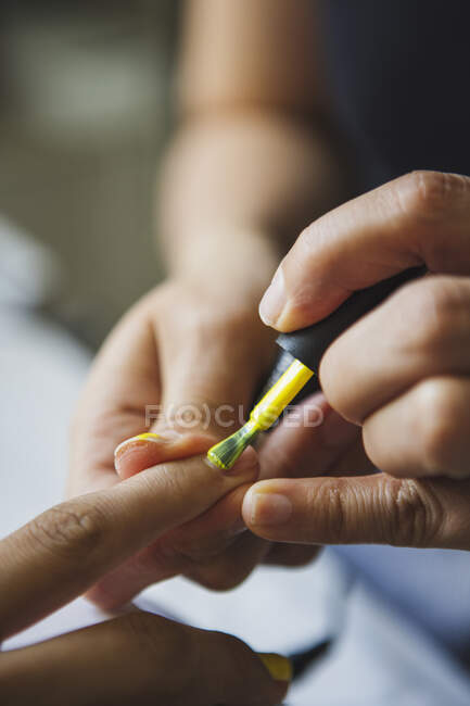 Crop female master applying yellow polish on nails of anonymous client in beauty salon — Foto stock