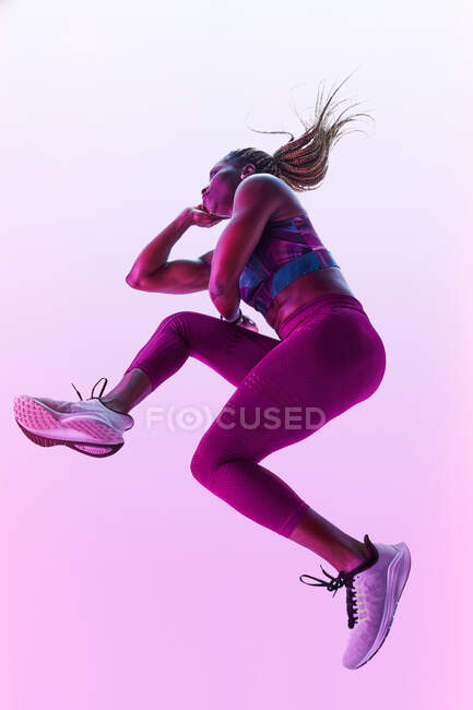 African American female athlete with flying hair in sports clothes jumping with clasped hands during training — Stock Photo