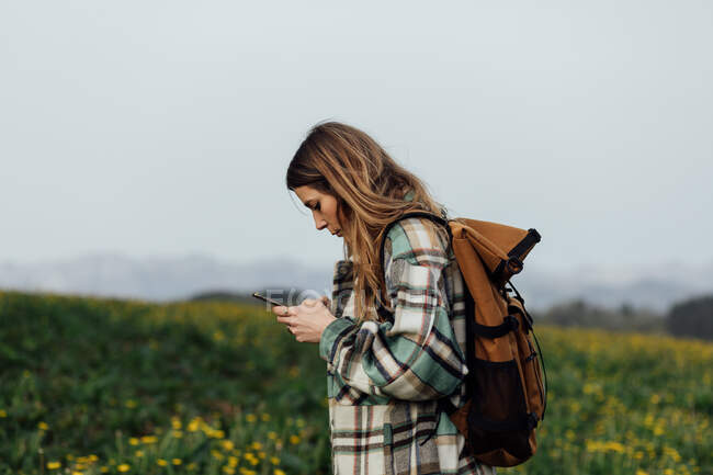 Вид збоку на жіночого пішохода, що використовує GPS-додаток на мобільний телефон, перебуваючи на лузі проти гір — стокове фото