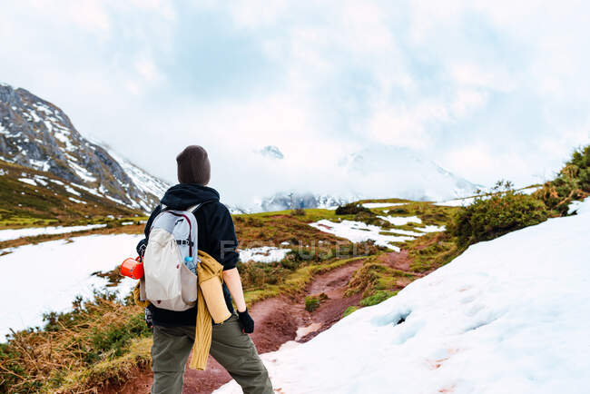 Vue arrière d'un touriste anonyme avec sac à dos debout sur une pelouse enneigée dans la vallée des montagnes des sommets d'Europe — Photo de stock