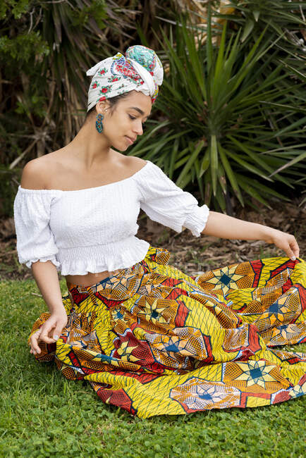 Cheerful young ethnic female in ornamental African skirt against palm plants on meadow — Stock Photo