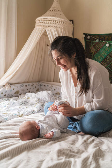 Sorrindo mãe interagindo com a criança irreconhecível na cama amassada em casa à luz do dia — Fotografia de Stock