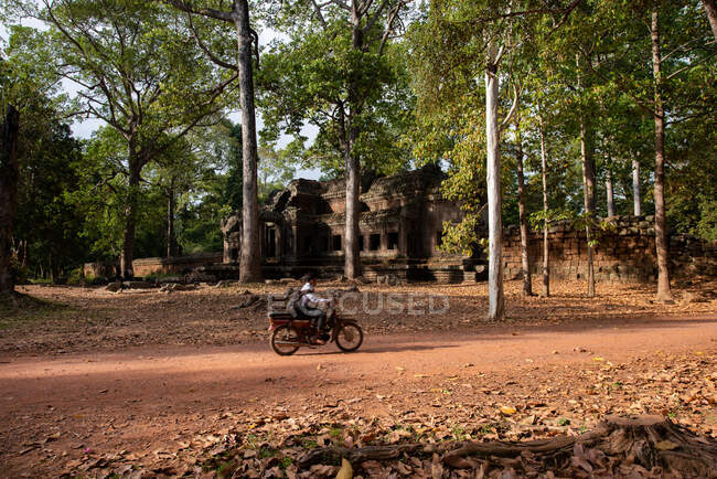 Seitenansicht eines anonymen männlichen Mopeds auf der Fahrbahn gegen betagte Gottesdienstbesucher und Bäume im kambodschanischen Angkor Wat — Stockfoto