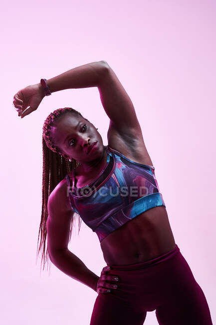 Muskulöse afroamerikanische Sportlerin in Activwear mit der Hand an der Hüfte, die seitlich beugt, während sie hocharbeitet und wegschaut — Stockfoto