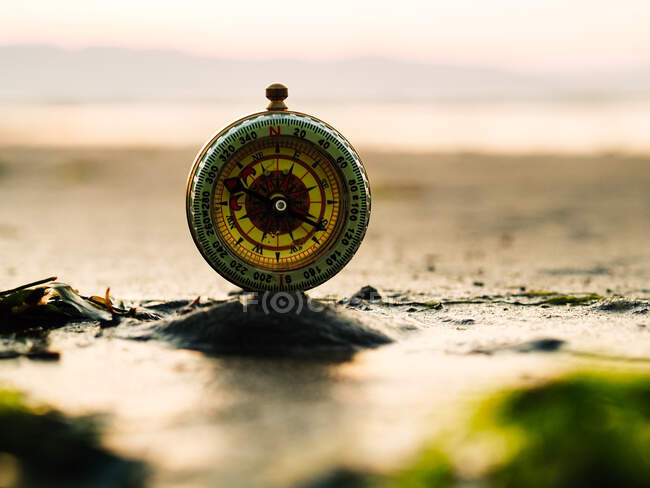 Selective focus of retro compass placed on sand against sea and mountains at sunset time - foto de stock