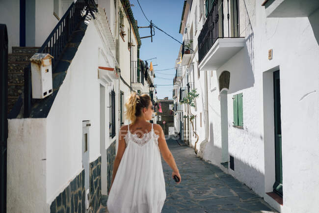 Вид ззаду татуйованого туриста-жінки, який дивиться на прогулянку між літніми фасадами житлового будинку на сонячному світлі — стокове фото