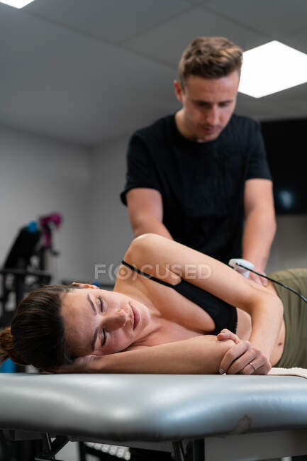 Männlicher Physiotherapeut, der während der medizinischen Behandlung im Krankenhaus Laser auf die Rückenhaut der Frau aufträgt — Stockfoto