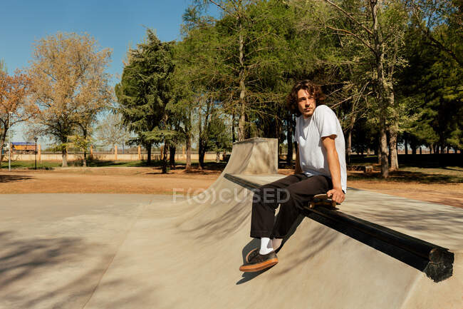 Junger Mann sitzt zum Ausruhen auf Skateboard — Stockfoto