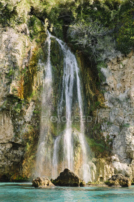 Удивительный вид на быстрый каскад, падающий с грубой скалы в бирюзовую волнистую лагуну в солнечную летнюю погоду в Малаге Испания — стоковое фото