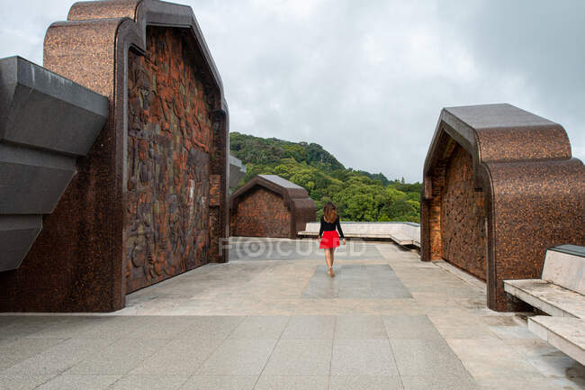 Back view of faceless female tourist strolling on tiled walkway between monuments against green mount in Thailand — Stock Photo