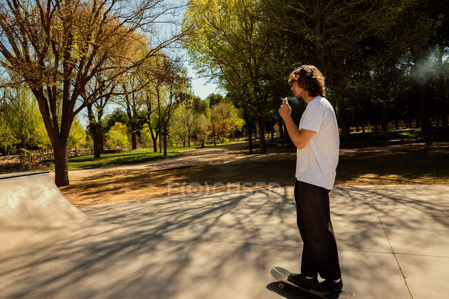 Skateboarder fumando mientras monta su tabla - foto de stock