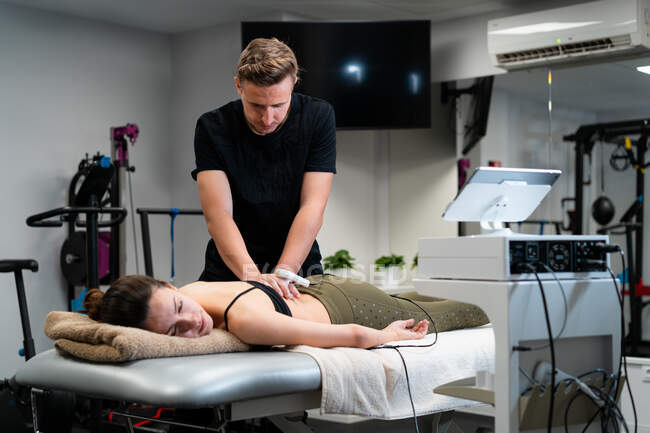 Чоловічий фізіотерапевт наносить лазер на шкіру спини жінки під час лікування в лікарні — стокове фото