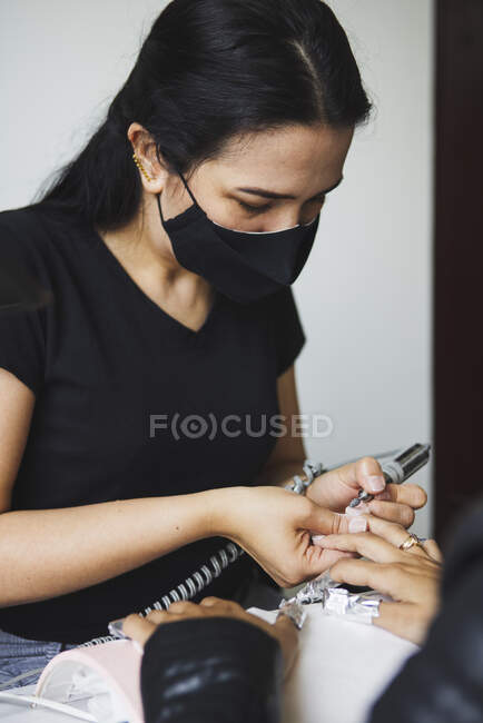 Female master using electric nail file while doing manicure for client in beauty salon — Stock Photo