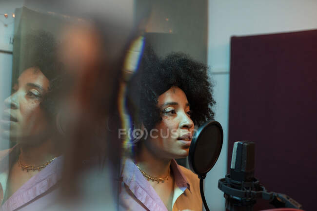 Schwarze Sängerin performt Song gegen Mikrofon mit Popfilter, während sie im Tonstudio steht und nach vorne blickt — Stockfoto